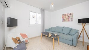 A modern living room with a light blue sofa, a small wooden coffee table, a white armchair, a television, and a ceiling light fixture. - GE Harbour Apartment 24 (Polis)