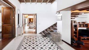 Un pasillo espacioso con alfombra estampada, suelo de madera, una escalera, un mueble para televisión y una cesta de mimbre.