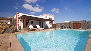 Un área de piscina con sillones de descanso y un edificio con un llamativo diseño rojo y blanco.