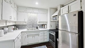 Une cuisine moderne avec des meubles blancs, un réfrigérateur en acier inoxydable, un four à micro-ondes et une cuisinière.