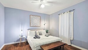 Une chambre à coucher comprenant un lit, une table de chevet, une lampe, un ventilateur de plafond et une fenêtre avec des rideaux.