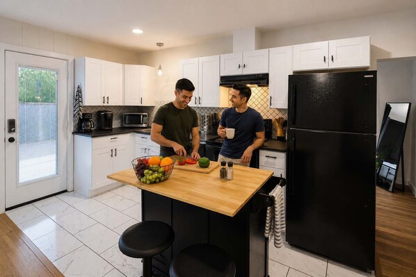 A modern kitchen with white cabinets, a black refrigerator, and a wooden island with a fruit bowl. - Delightful 1BR 1BA Cozy Flat (Fort Worth)