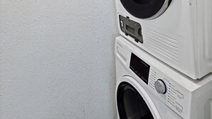 Een gestapelde wasmachine en droger in een wasserij met een effen witte muur.