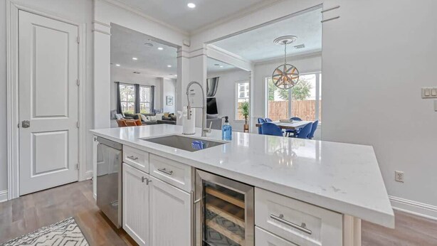Une cuisine moderne avec des meubles blancs, un grand îlot central doté d’un évier et un coin repas visible à travers une porte ouverte.