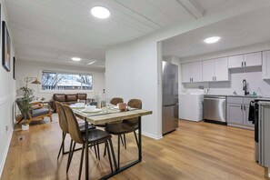 Une cuisine moderne dotée d’appareils électroménagers en acier inoxydable, un coin repas avec une table et des chaises en bois, et une vue sur l’extérieur.