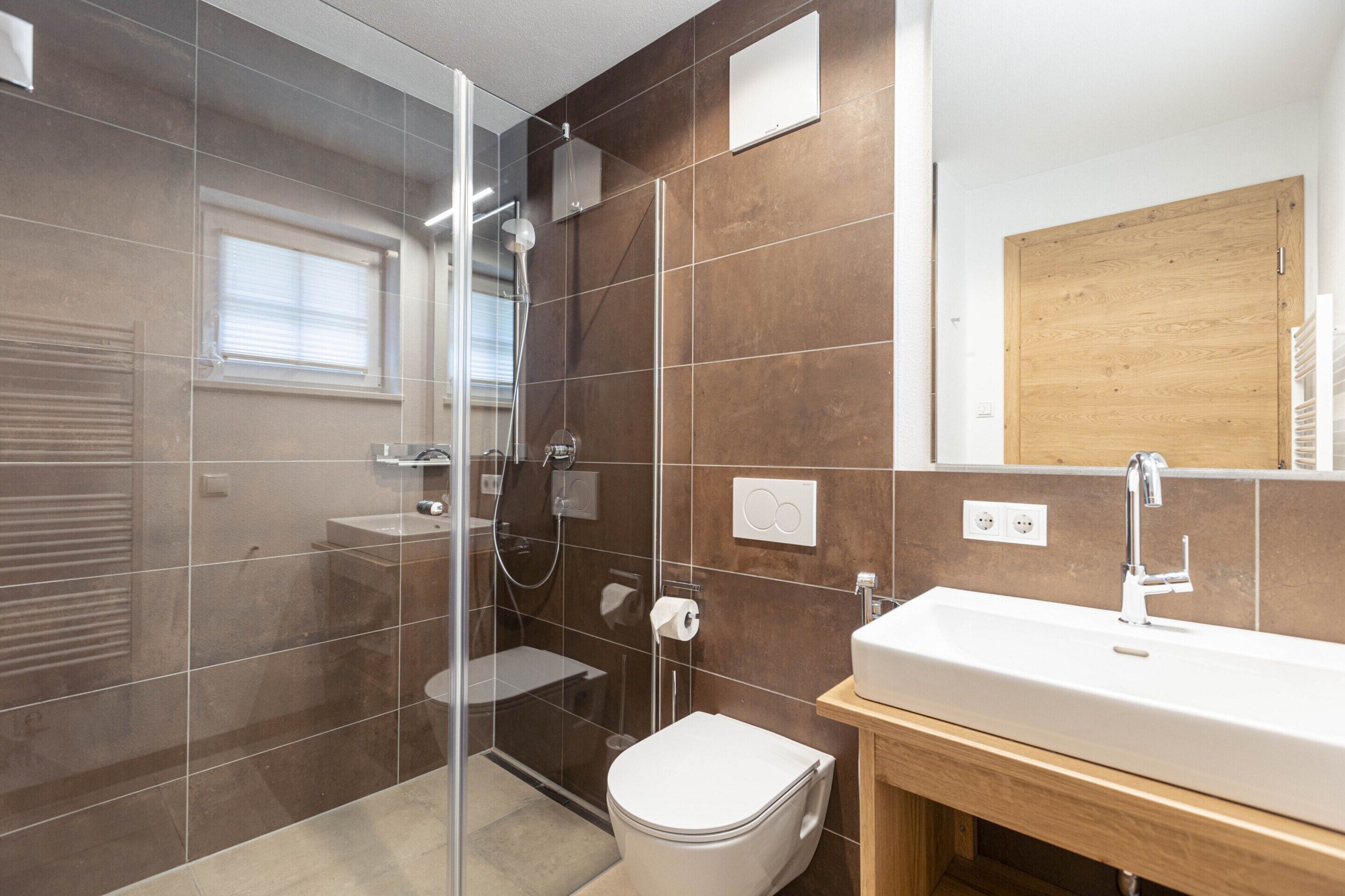 A modern bathroom with a glass shower enclosure, a white toilet, and a wooden vanity with a sink.