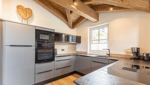 A modern kitchen with grey cabinets, a built-in oven, and a large island with a sink. - Superior Ferienhaus # 2B mit Sauna (Uttendorf)