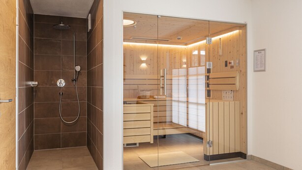 A modern bathroom with a glass shower enclosure, wooden cabinets, and a small sink area. - Superior Ferienhaus # 2B mit Sauna (Uttendorf)