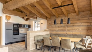 A modern kitchen with wooden beams, a built-in bench, and a dining area with chairs and a table. - Superior Ferienhaus # 2B mit Sauna (Uttendorf)