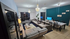 A modern living room with a sofa set, a dining table, and a TV. - SEASIDE HOSTELS (Dubai)
