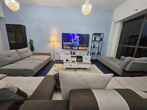 Ein modernes Wohnzimmer mit grauen Sofas, einem Flachbildfernseher, einem Couchtisch und dekorativer Beleuchtung.