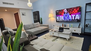 A modern living room with a grey sofa, a white coffee table, and a TV displaying 'KOLITA'. - SEASIDE HOSTELS (Dubai)