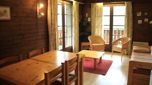 A wooden interior with a dining table, chairs, a sofa, and a television.