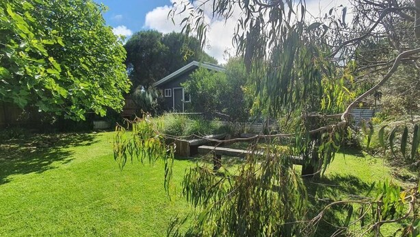Un giardino curato con prato, recinzione in legno e una casa sullo sfondo.