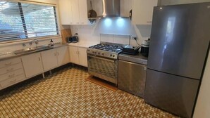 Una cucina con mobili bianchi, piano cottura a gas, frigorifero in acciaio inossidabile e pavimento piastrellato.
