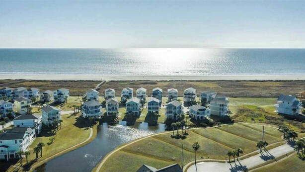 Una zona residenziale costiera con case disposte a file lungo una spiaggia, un piccolo canale navigabile e una vista aperta sull'oceano.