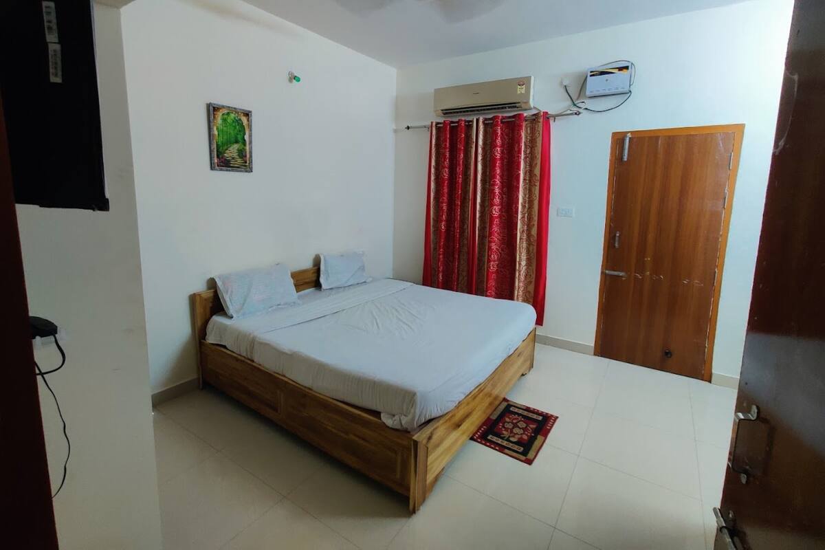 Une chambre à coucher avec un lit en bois, un climatiseur, un rideau rouge et une porte.