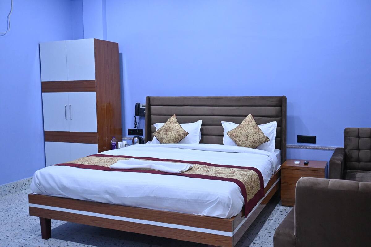 A hotel room with a bed, a wardrobe, a desk with a phone, a chair, and a nightstand.