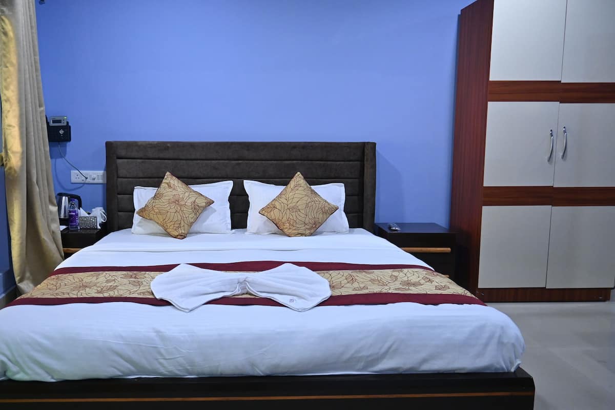 A neatly made bed with white linens and two decorative pillows, a wooden headboard, and a bedside table with a remote control.