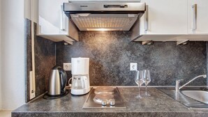 Una cocina moderna con estufa integrada, cafetera y copas de vino sobre la encimera.