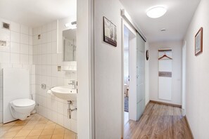 Une salle de bain avec des carreaux blancs, des toilettes, un lavabo et un miroir.
