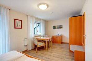 Een kamer met een bed, een tafel met stoelen, een klein kastje en een raam met gordijnen.
