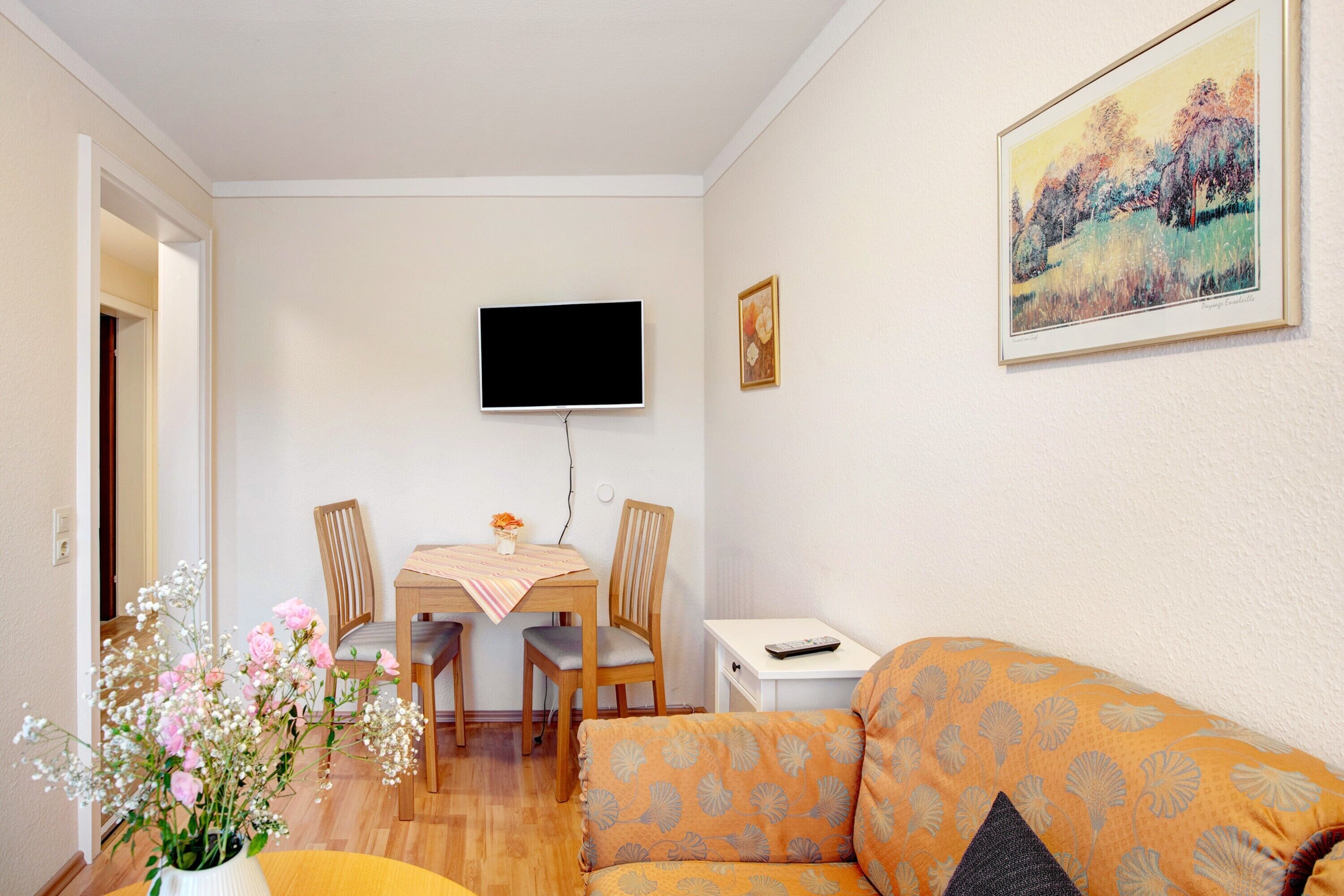 A living room with a sofa, a dining table with chairs, a flat-screen TV mounted on the wall, and a painting on the wall.