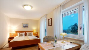 Habitación de hotel con cama doble, escritorio con lámpara, silla y ventana con vistas.