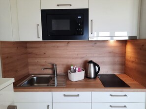 Una cocina con un lavamanos de acero inoxidable, microondas, hervidor y un panel trasero de madera.