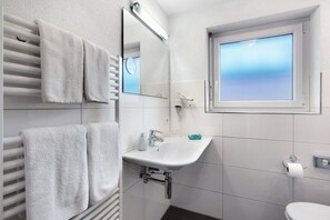 A modern bathroom with a white sink, towel rack, and a window with blinds. - Apartment '1' with Shared Terrace, Shared Garden and Wi-Fi (Bad Bellingen)