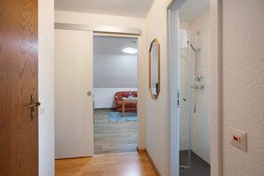 A hallway leading to a bedroom with a bed, a bathroom with a shower, and a small table with a chair. - Apartment No. 4 with 2 Rooms and Balcony (Bad Bellingen)