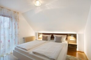 Un dormitorio con dos camas, una mesita de noche, una lámpara de techo y un ventanal con cortinas.
