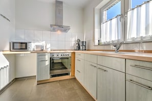 Eine Küche mit Mikrowelle, Toaster, Kaffeemaschine, Backofen und einem Fenster mit Vorhängen.