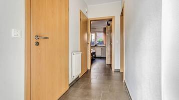 A hallway with a wooden door, a radiator, and a view into a kitchen area.