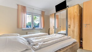 Een slaapkamer met twee bedden, een garderobe, een televisie en een raam met gordijnen.