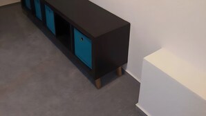 A room with a long black bench, a white wall with geometric patterns, and a grey floor. - Brendle Apartment with Balcony and Wi-Fi (Sankt Johann)