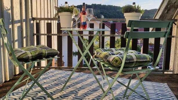 A patio with two green chairs, a small table, and a bottle of wine. - Brendle Apartment with Balcony and Wi-Fi (Sankt Johann)
