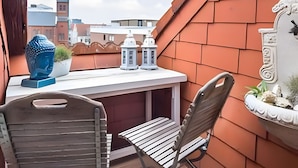 A rooftop terrace with a table and two chairs, a blue sculpture, and a white planter with plants. - Apartment 'Am Alten Rathaus' with Balcony and Wi-Fi (Norderney)