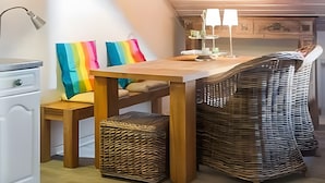 A cozy room with a wooden ceiling, a dining table, a wicker chair, a colorful pillow, and a small white cabinet. - Apartment 'Am Alten Rathaus' with Balcony and Wi-Fi (Norderney)