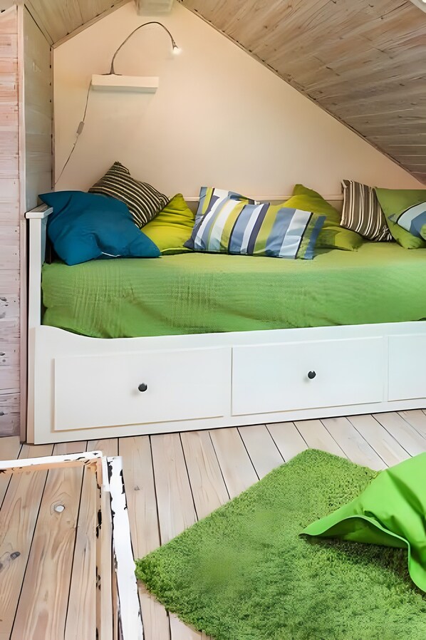 A loft-style bedroom with a sloped ceiling, a white bed with multiple pillows, a green area rug, and a small white nightstand.