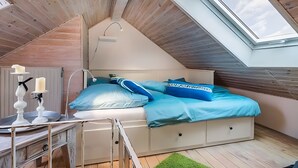 A loft-style bedroom with a sloped ceiling, a skylight, a bed with blue bedding, a bedside table with candles, and a green rug. - Apartment 'Am Alten Rathaus' with Balcony and Wi-Fi (Norderney)