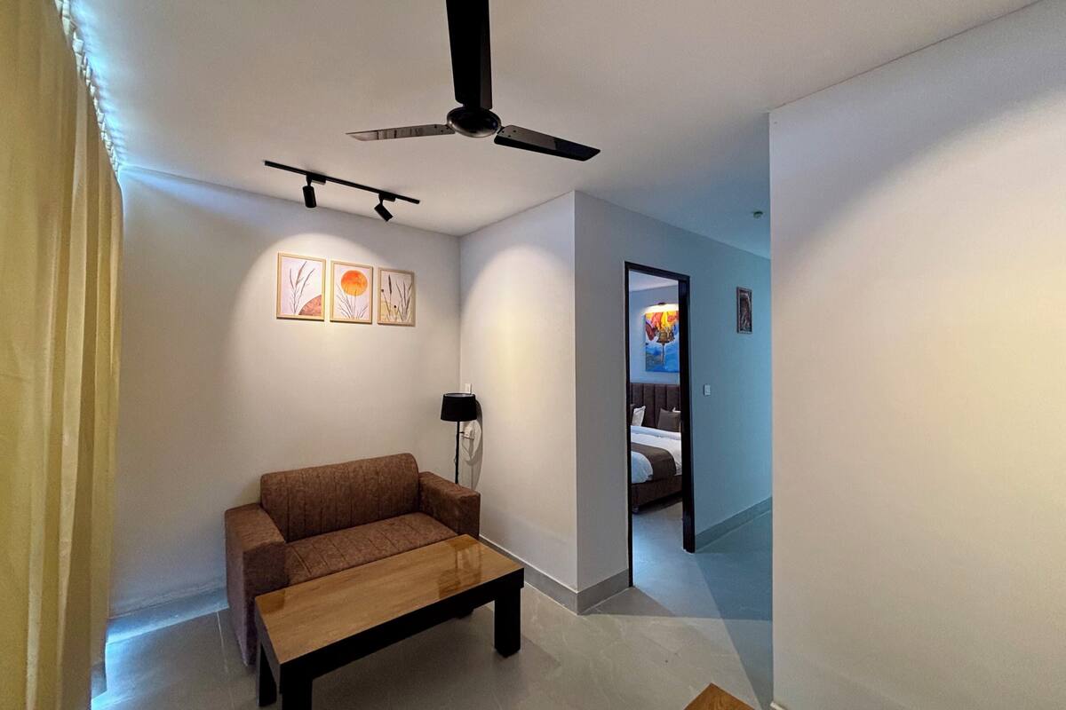 A modern living room with a ceiling fan, a sofa, a coffee table, and a hallway leading to a bedroom.
