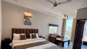 Um quarto espaçoso com uma cama grande, um ventilador de teto, uma mesa de cabeceira, um sofá e uma janela com vista.