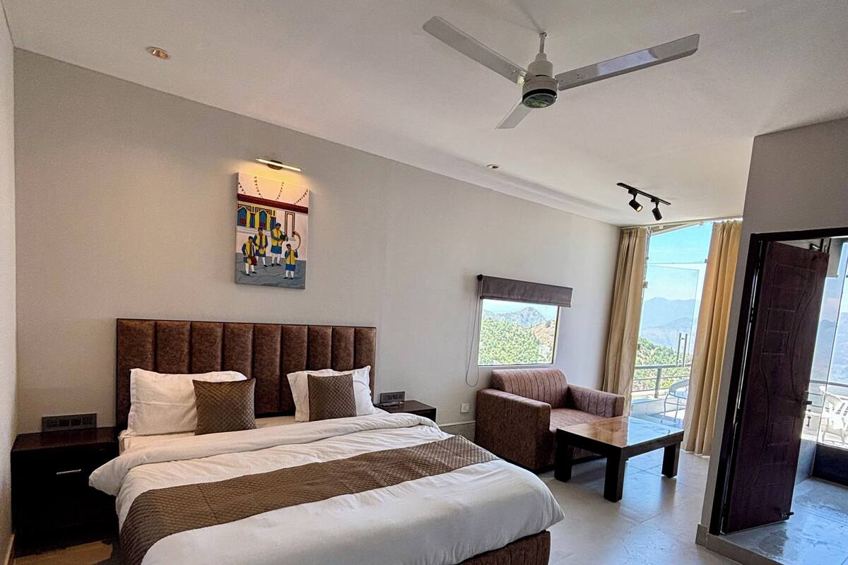 A spacious bedroom with a large bed, a ceiling fan, a nightstand, a sofa, and a window with a view.