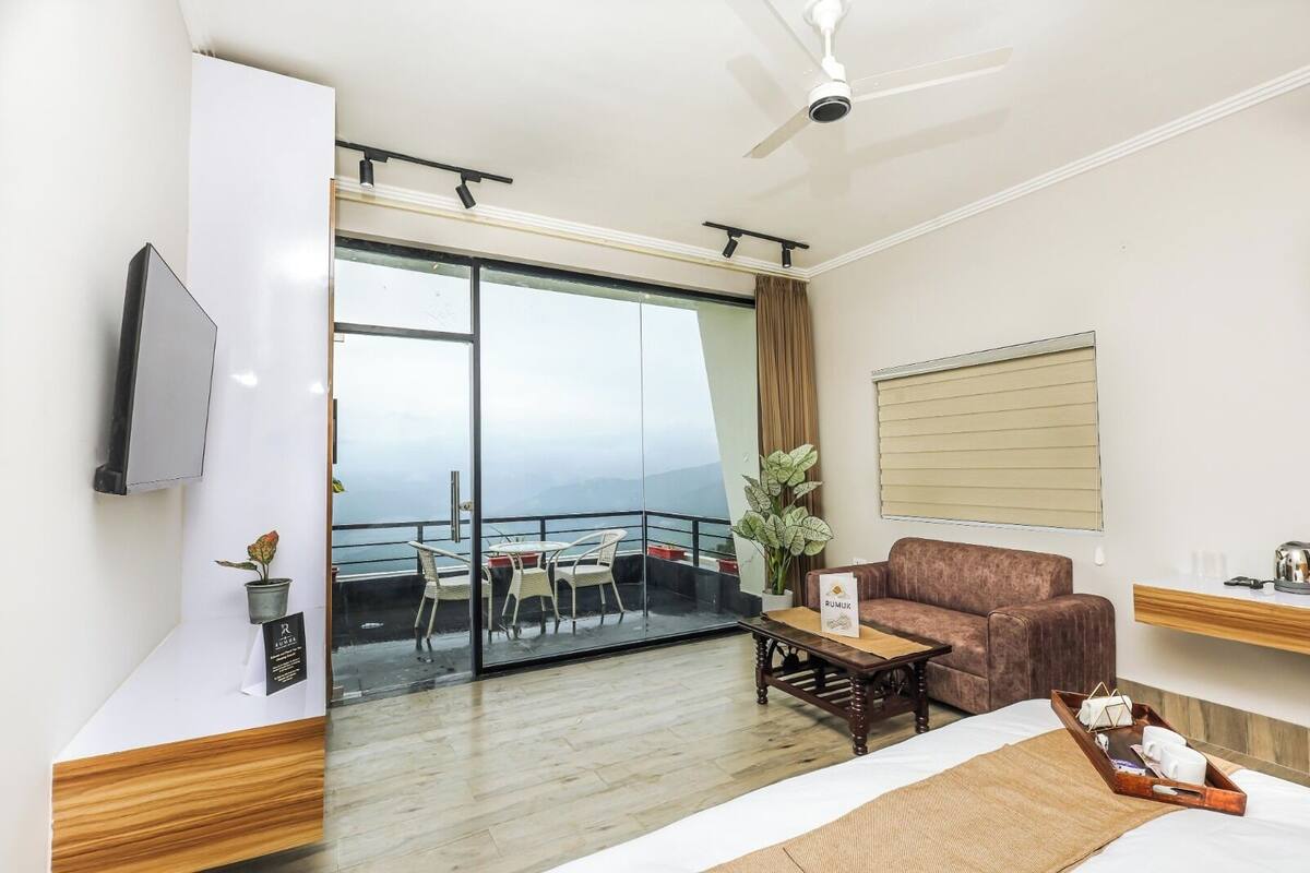 A hotel room with a balcony, a sofa, a coffee table, a TV, and a window with blinds.