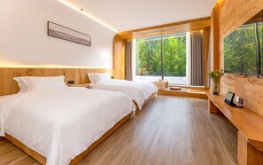 A modern hotel room with two beds, wooden flooring, large windows with curtains, and a wooden bench with a vase.