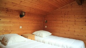 Dormitorio de cabaña de madera con dos camas, una mesita de noche y una linterna fijada a la pared.