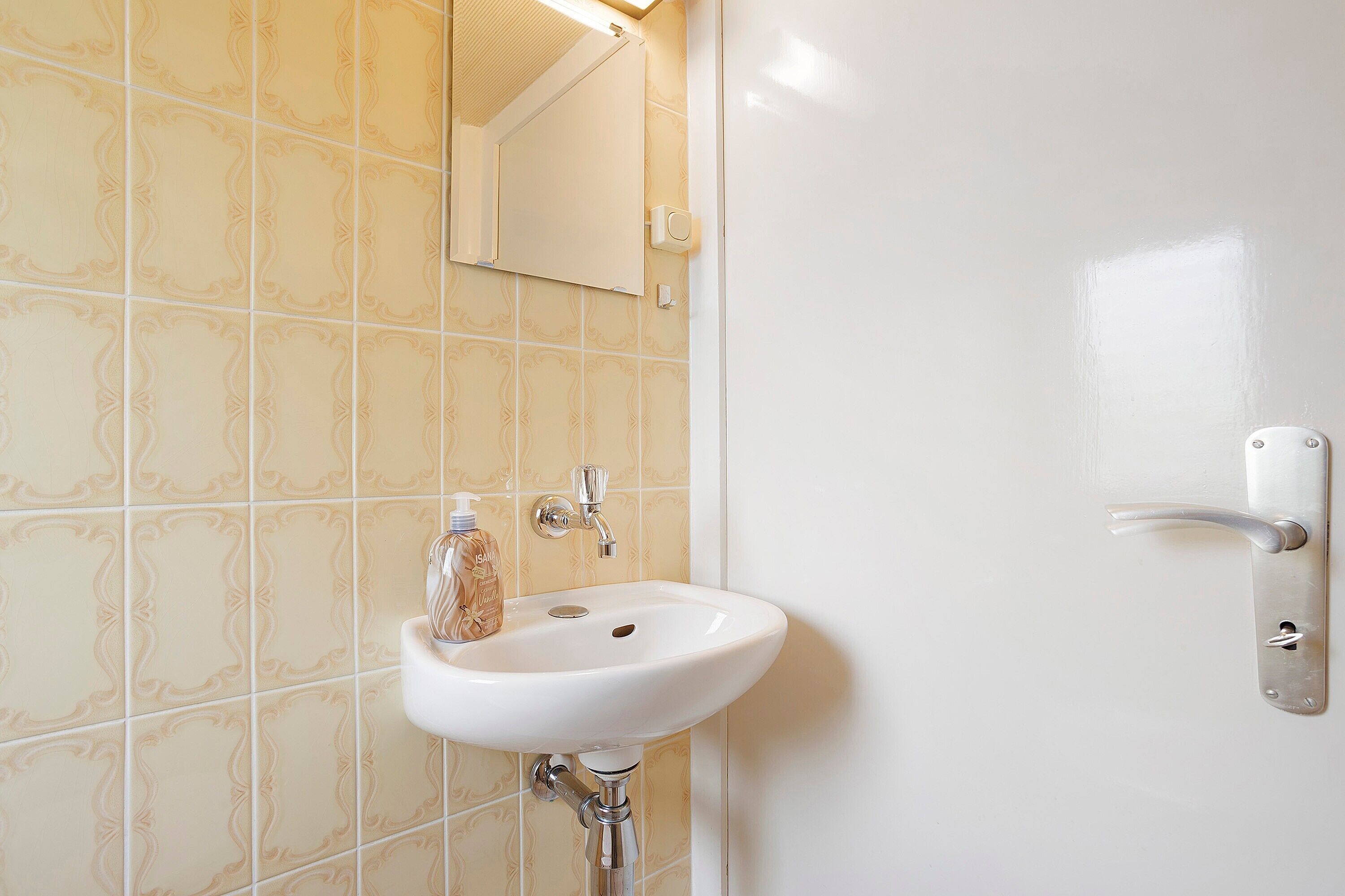 Ein Badezimmer mit einem weißen Waschbecken, einem Spiegel und einer Tür mit Griff.