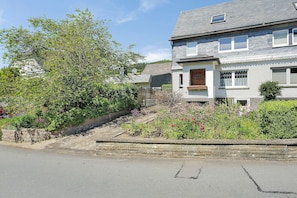 A residential building with a stone retaining wall, a small garden with flowers, and a clear sky.