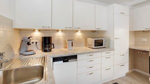 A modern kitchen with white cabinets, a stainless steel sink, a coffee maker, a microwave, and a dishwasher.